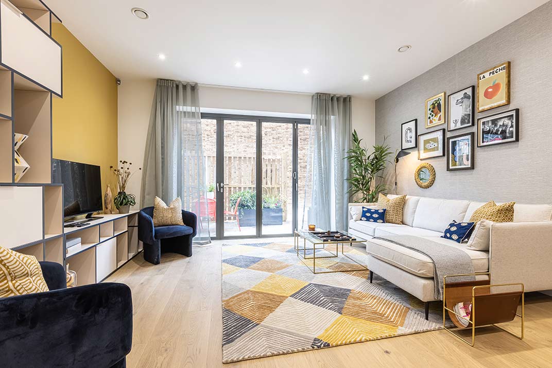 Modern living room with a large glass door, geometric rug, white sofa, wall art, TV, and decorative plants, featuring neutral and yellow accents.